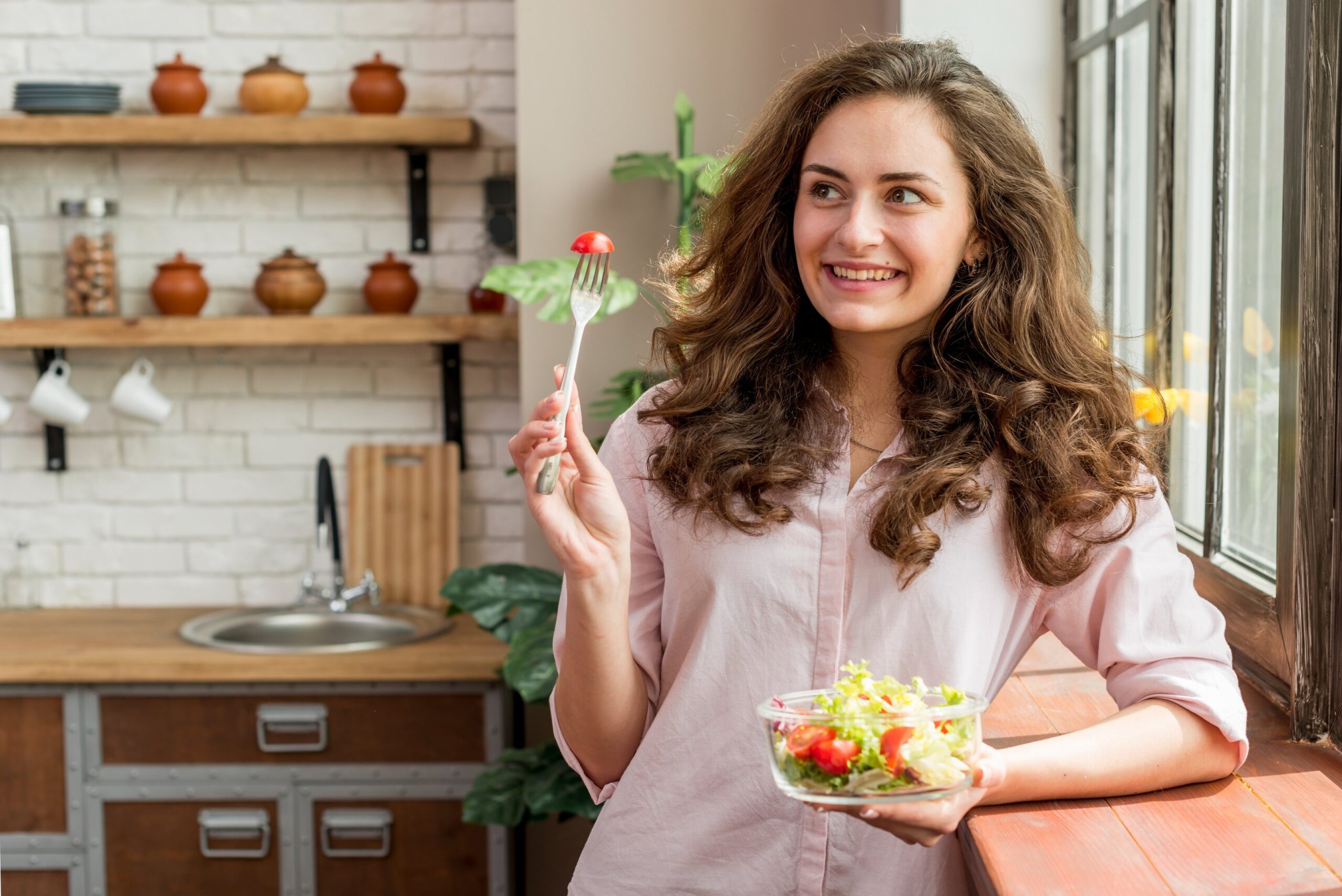 A happy women standing in her kitchen holding a salad bowl. 