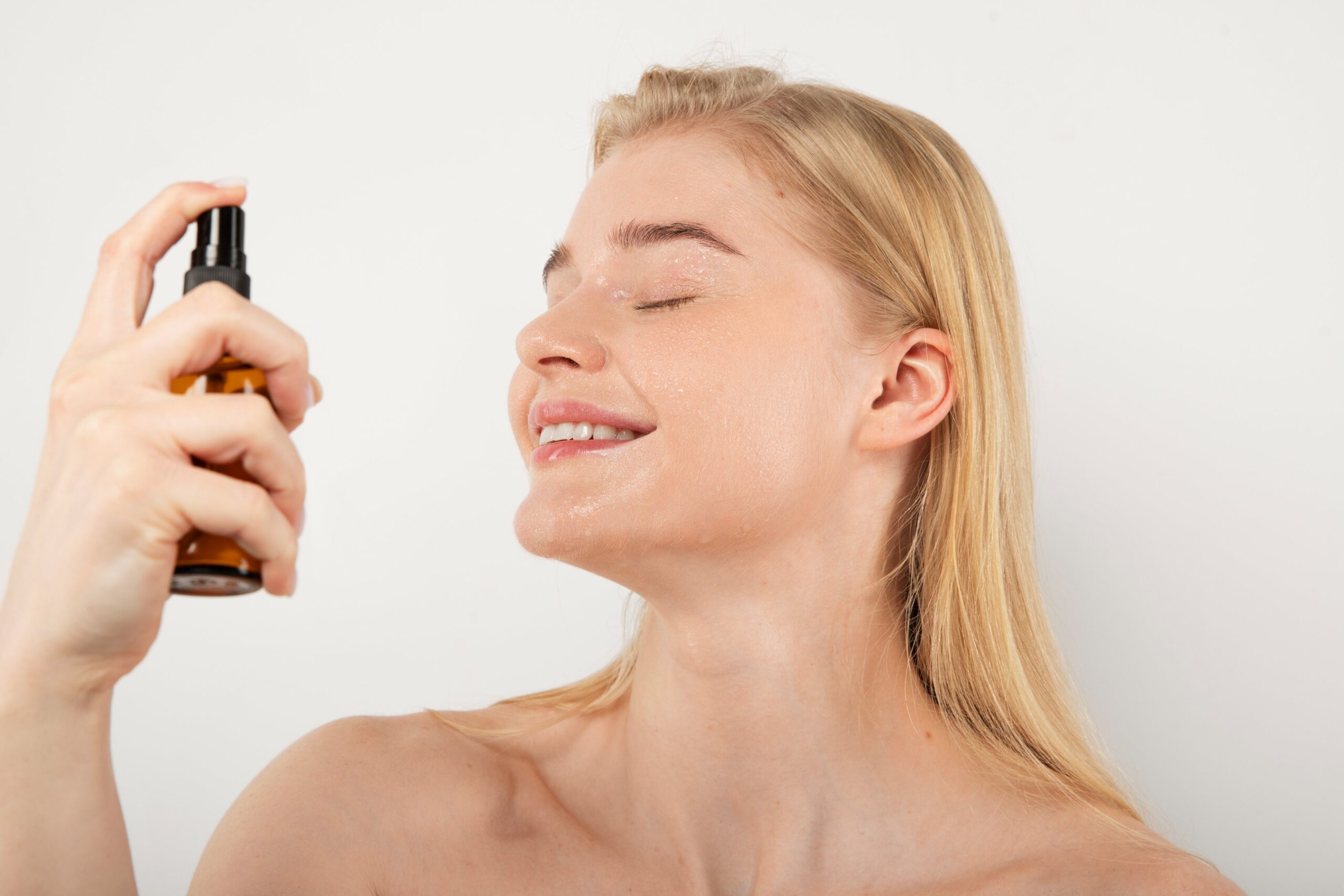 A girl  happily spraying serum on her face to get brighter skin.