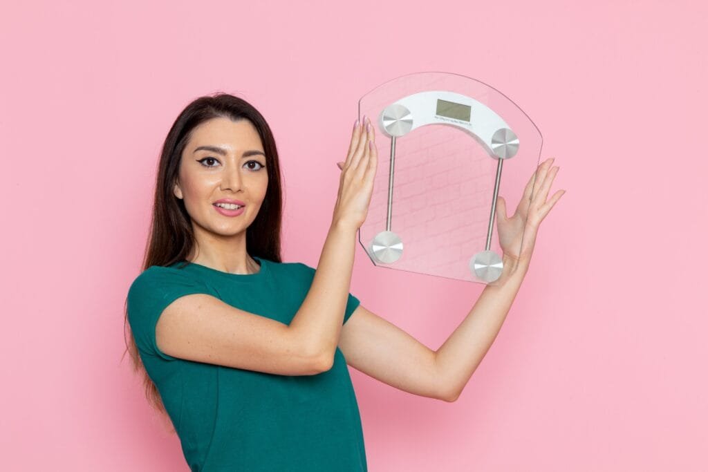 front view young female green t shirt holding scales pink wall waist exercise workout beauty slim female sport Yg2jO2E5n6i2zgNp